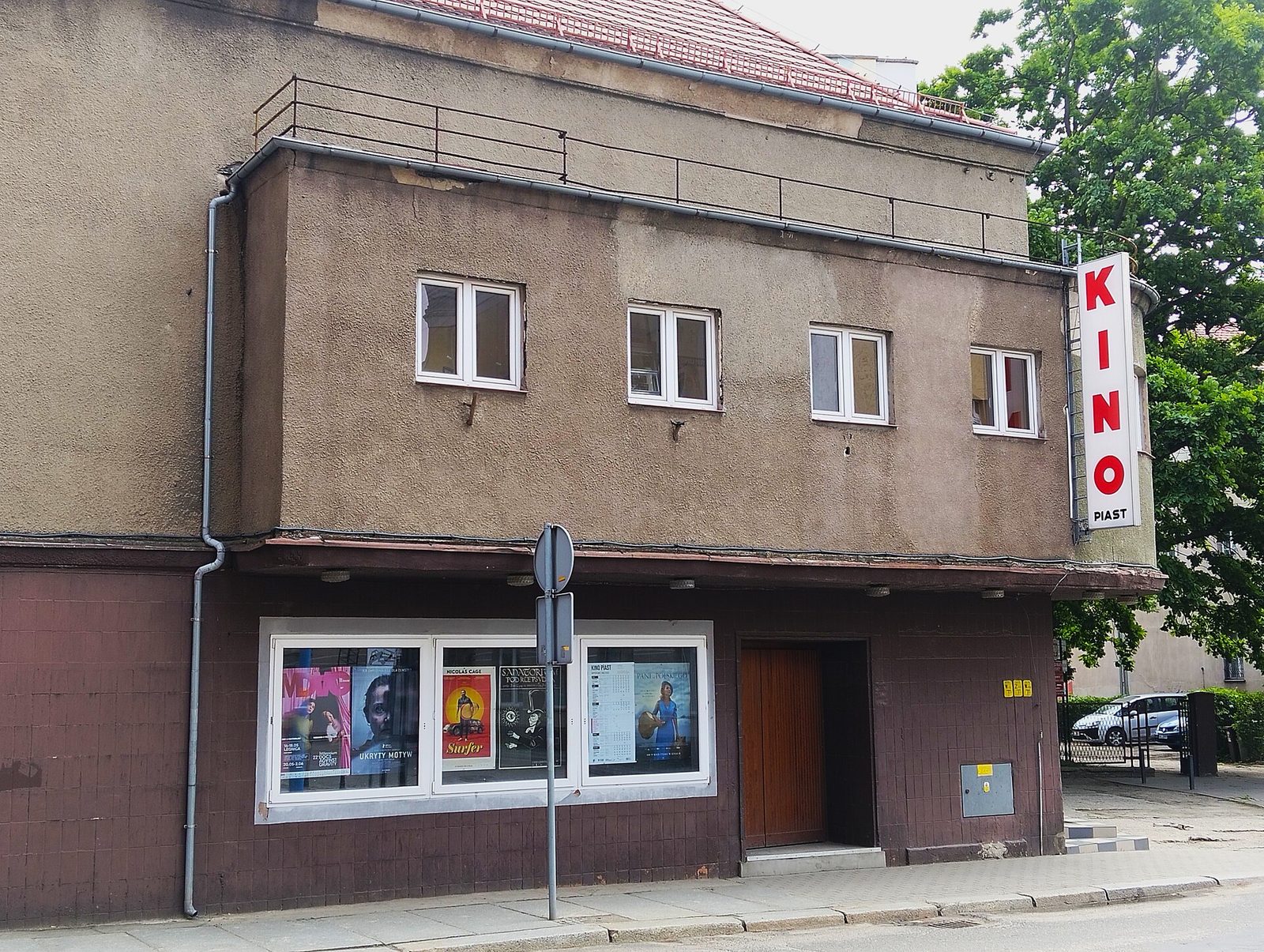 Budynek kina Piast w Legnicy z pionowym czerwonym neonem Kino i plakatami filmowymi w witrynie