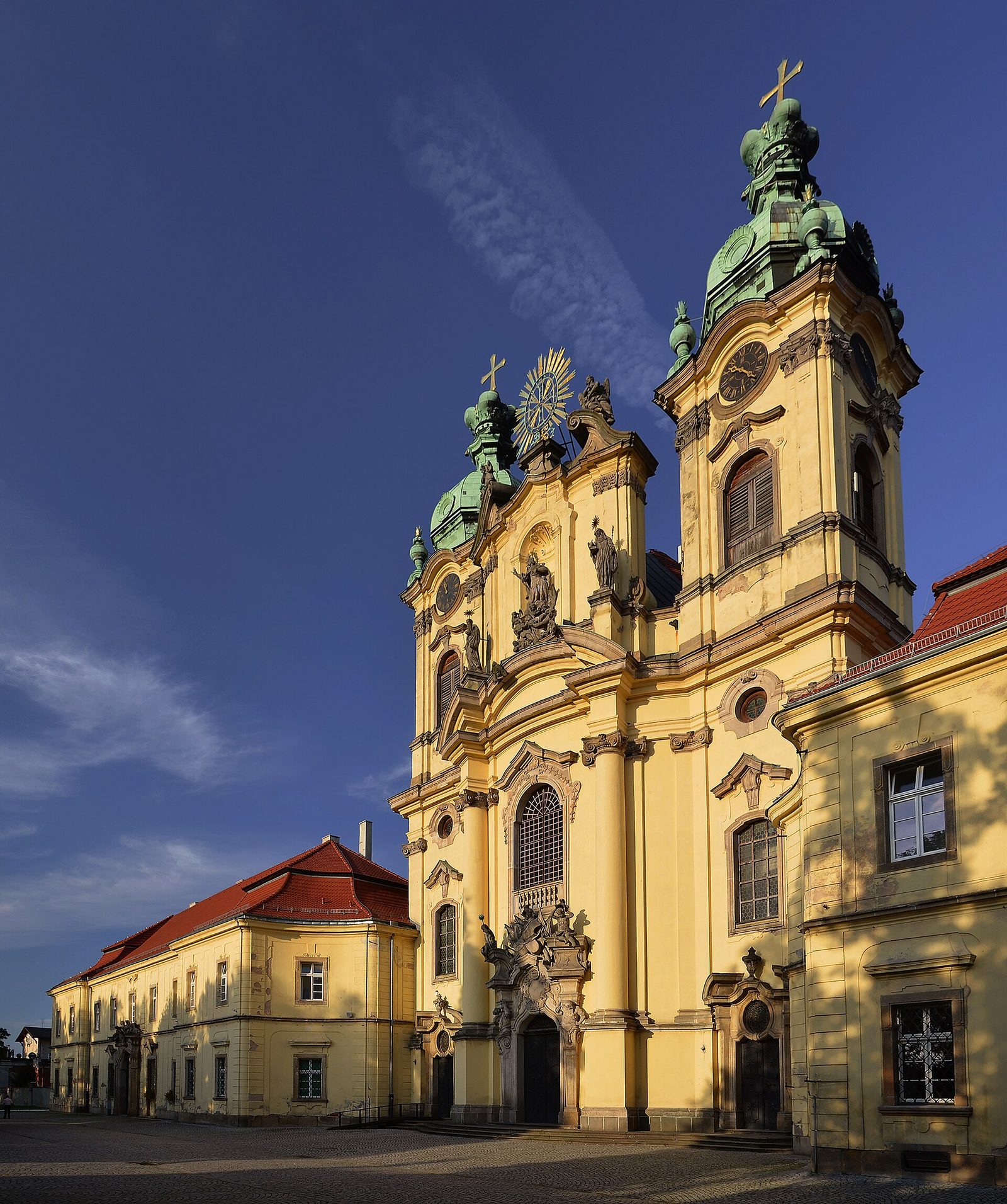 Barokowa fasada bazyliki św. Jadwigi w Legnickim Polu z dwiema wieżami o zielonych hełmach, obok żółte skrzydła dawnego klasztoru